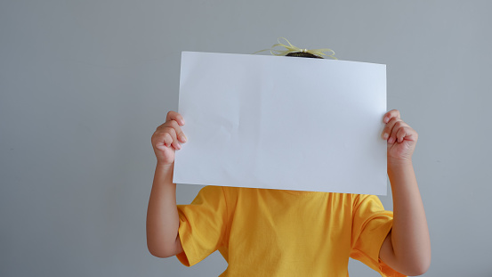 Portrait of a young asian little girl holding white paper blank sign over gray background
