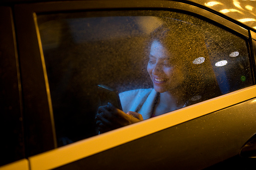 Young woman messaging on mobile phone while sitting on back seat of car at night