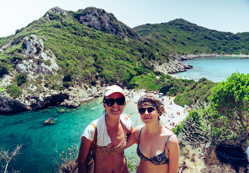 Two women in a swimsuits posing for a portrait. Enjoying hot summer weather and beautiful sun. Beautiful view in the mountains with a lagoon