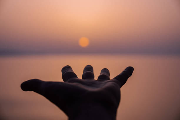 Reaching for the sun. Hand grabbing the setting orange sun stock photo