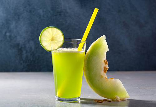 Fresh Honeydew Melon (Cucumis melo Inodorus) juice on a dark blue background with a slice of lime; copy space