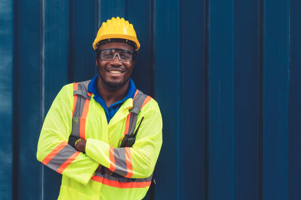 joven trabajador afroamericano en un patio de contenedores de envío en el extranjero. gestión logística de la cadena de suministro y concepto de exportación internacional de mercancías. - industrial ship dock worker engineer harbor fotografías e imágenes de stock