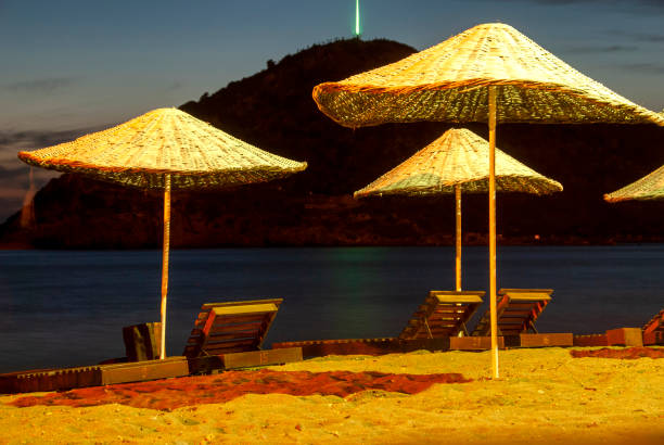 Night on the beach. Turkish flag and Sun beds under straw umbrellas in Gümüşlük, Bodrum, Turkey
