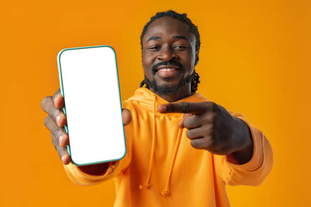 istock Smiling african man pointing at cellphone with blank screen with copy space 1465887907