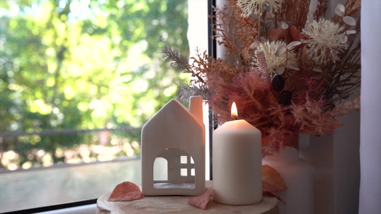 Still life details in home on a wooden window. Autumn decor on a window, dried flowers, candle and toy house