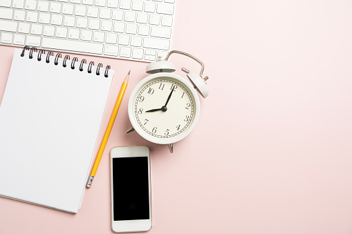 close up of workspace desk with alarm clock, notebook, computer keyboard pink table background with copy space, minimal style, for creative flat lay concept