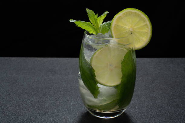 a glass of mojito cocktail on a dark background a glass of mojito cocktail on a dark background soda water glass lemon stock pictures, royalty-free photos & images