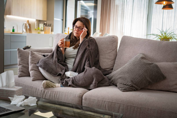 istock Sick woman with flu and headache sitting on sofa 1465897764