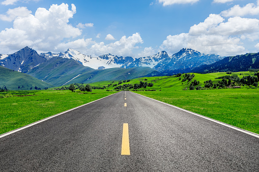 Straight asphalt road and green grass with snow mountain nature landscape in Xinjiang, China.