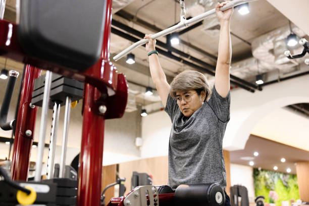 donna di mezza età che esercita utilizzare una macchina lat pulldown in palestra. - women weight bench exercising weightlifting foto e immagini stock