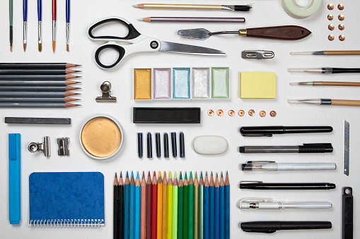 Stationery set flat lay on white background. Creative school, or student, artist, designer desk. Variety of equipment as paint, pencils, scissors, pens and more view from above.