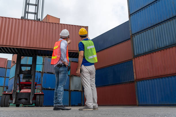 istock Industrial worker works with co-worker at overseas shipping container yard . Logistics supply chain management and international goods export concept . 1465910347