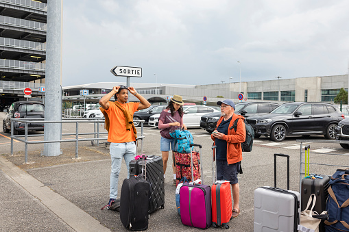 A group of people standing in a rental car car park at an airport in Toulouse, France. They are waiting to be seen to and are standing with their suitcases after getting off a flight.