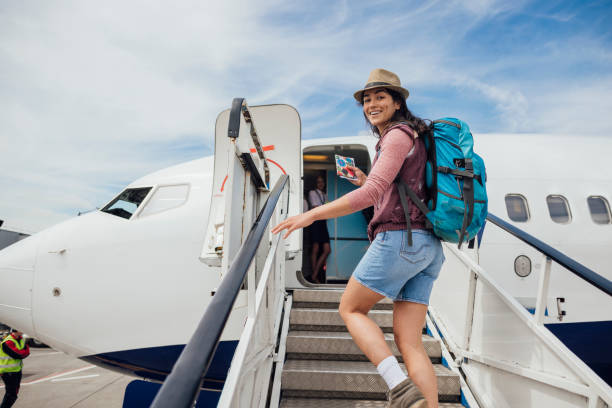 The Way to the Plane A young woman walking up steps while getting ready to board a plane at the airport in Toulouse, France. She is walking while looking back at the camera and smiling. passenger stock pictures, royalty-free photos & images