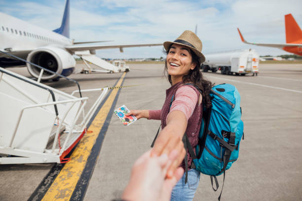 Are You Ready for This? A personal perspective of a young woman walking outdoors on an airport tarmac in Toulouse, France while looking over her shoulder at the camera and smiling. She is holding hands with an unrecognisable person and leading them to the plane. reach destination stock pictures, royalty-free photos & images