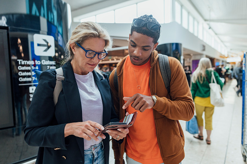 A mature woman asking a young man for directions to her departure gate in an airport in Toulouse, France. She is looking at her phone while he helps her with directions.