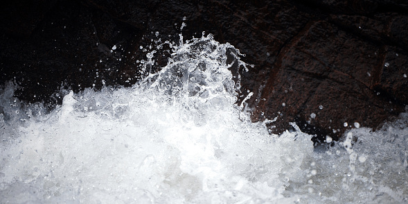 Water Drops after splash. Splashing of the mountain river against the dark rocks. Splashes of clear water in the rapids. Drops in the air, the power of the river. natural background, clear water.