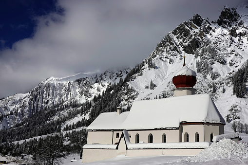The small snowcovered church of Stuben the skiresort of St Anton am Arlberg on a sunny afternoon with mountainrange in the background in the Arlberg Alps in Austria