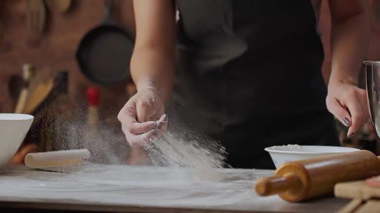 Slow motion view of Hispanic young woman spreading flour on a table for bread baking in a rustic kitchen