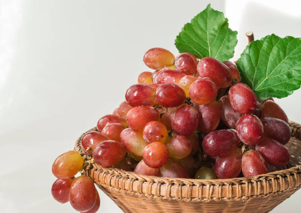 Sweet fresh organic red grapes in wooden basket and green leaves