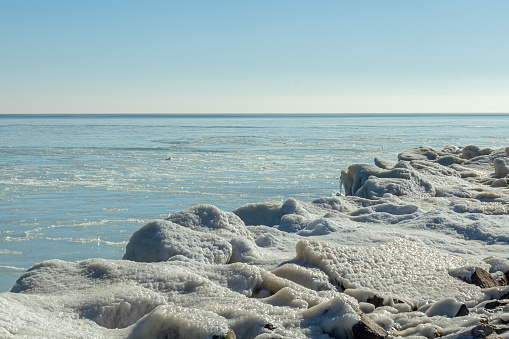 Close-up of the icy seashore, frozen waves, rocks and sun glare on the ice.