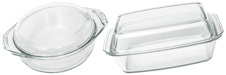 Studio shot of large round and oblong empty clear glass casserole baking pans, covered with lids, isolated on white background, side view.