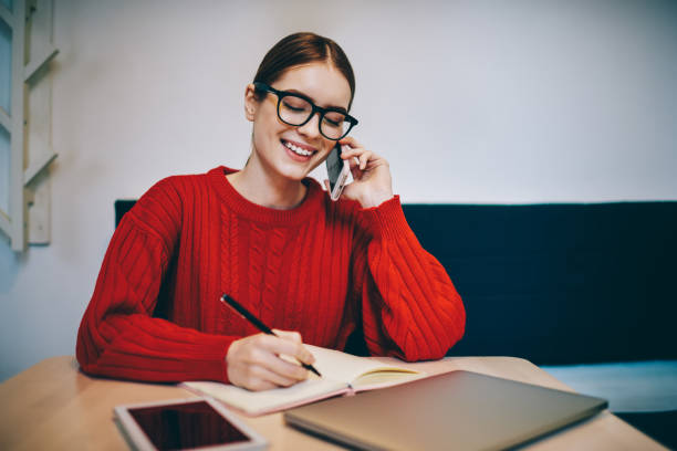 istock Smiling female teleworker writing in notebook and speaking on smartphone 1465947178