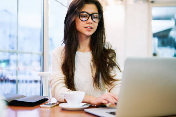 istock Positive young woman working on laptop in cafe 1465948462