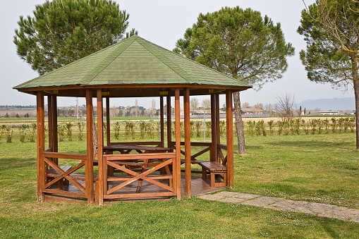 Wooden gazebos with picnic table and wooden bench in a green mowed lawn