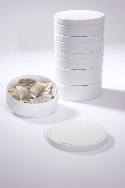 Closeup of a white Swedish snus can and portion snuff pouches against a white background stock photo