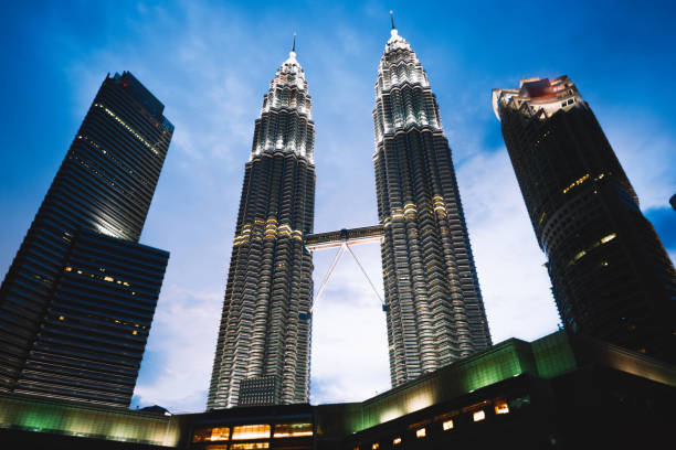 From below of modern building of Petronas Twin Towers located in Kuala Lumpur in Malaysia with skyscrapers on sides under sky