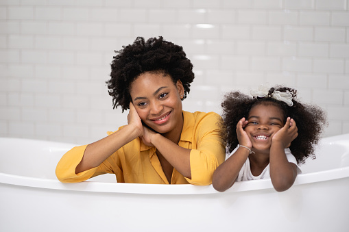 African american family, happy mother and baby daughter having fun and playing together at the bathroom, white wall backgroung