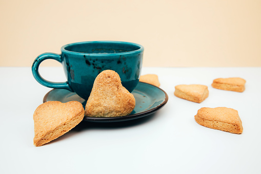 A cup of coffee with a plate with heart-shaped shortbread cookies on a white background. Front view