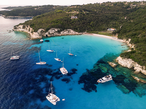 Group of sailboats and yachts anchored in bay with amazing beach. Crystal clear water has a beautiful color. Aerial view of Voutumni beach, Antipaxos island, Greece