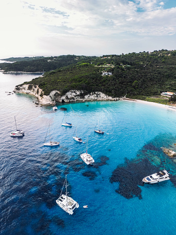Group of sailboats and yachts anchored in bay with amazing beach. Crystal clear water has a beautiful color. Aerial view of Voutumni beach, Antipaxos island, Greece