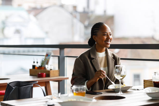 Black woman in restaurant A beautiful African-American woman is sitting on the restaurant's balcony, enjoying Italian pasta and a glass of white wine. She talks to someone who is not in the photo. georgijevic stock pictures, royalty-free photos & images