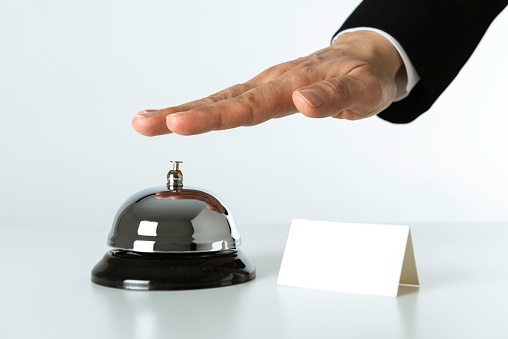 Hotel servants hand is ringing a service bell on white background. On the right of the bell is a white empty card. Only the hand is visible of the hotel servant.