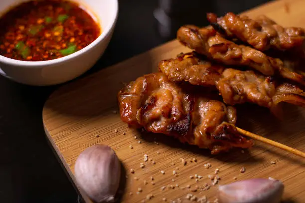 Photo of Grilled pork,mooping and spicy sauce on a wooden chopping board, decorated with garlic and roasted rice