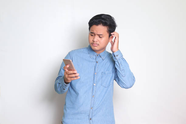istock Asian man holding mobile phone with sad expression on face while scratching forehead 1465977053
