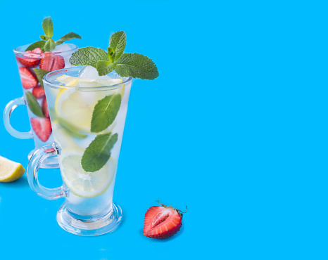 Infused or detox water with strawberry, lemon and mint in the drinking glasses on the blue background. Copy space. Close-up.