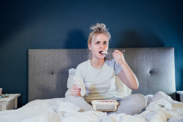 istock Shocked, stressed, surprised woman eating ice cream, holding a remote control while watching TV in bed. Scary horror movie or terrible news, scare in her eyes Overeating, Jamming of negative emotions 1465998462