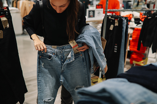 Woman in mid 30s goes shopping for denim jeans in a mall or a clothing store.
