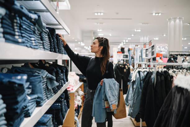 mujer comprando jeans vaqueros en una tienda de ropa - mercancía fotografías e imágenes de stock