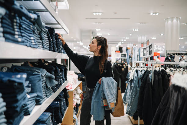 mulher que compra jeans jeans em uma loja de roupas - mercadoria - fotografias e filmes do acervo