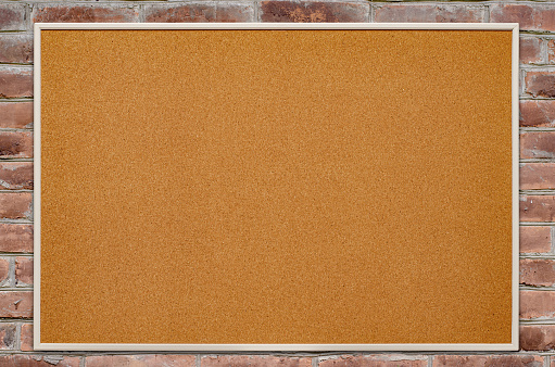 An empty cork board is hanging on a brick wall. Copy space