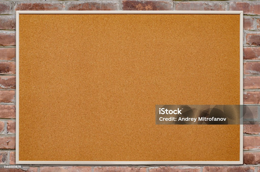 An empty cork board is hanging on a brick wall. Copy space. An empty cork board is hanging on a brick wall. Copy space Bulletin Board Stock Photo