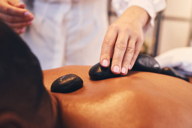 manos, piedras calientes y masaje con un hombre en un spa, acostado en una mesa o cama para aliviar el estrés y el bienestar. relájese, disfrute del lujo y rockee con un cliente masculino en un salón de salud para fisioterapia - lastone therapy men spa treatment male fotografías e imágenes de stock