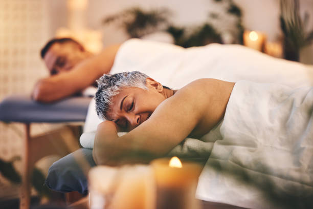 massaggio donna, spa e coppia per relax, pace e benessere skincare in località di villeggiatura. signora calma, matura e addormentata sul letto del salone di lusso con partner per terapia ricca, guarigione zen o cosmetici per il corpo - spa treatment health spa massaging couple foto e immagini stock