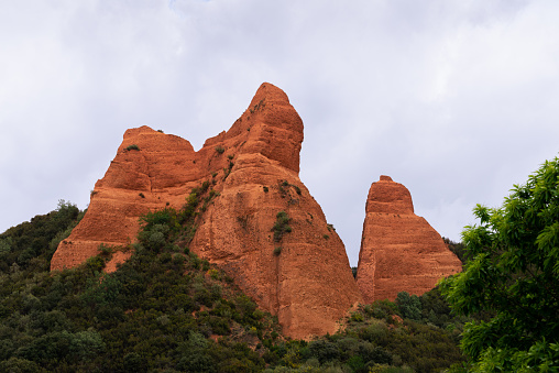 View of a peak in Las Médulas natural park, old Roman mines, León (Spain). Spanish landscape environment formed by an old Roman gold mine in the region of El Bierzo, province of León, autonomous community of Castilla y León. Landscape of reddish sands, nowadays partially covered by chestnut and oak vegetation.