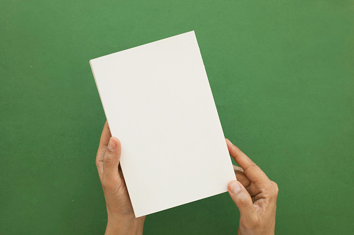 Cropped hands of man holding blank book against blue background.
